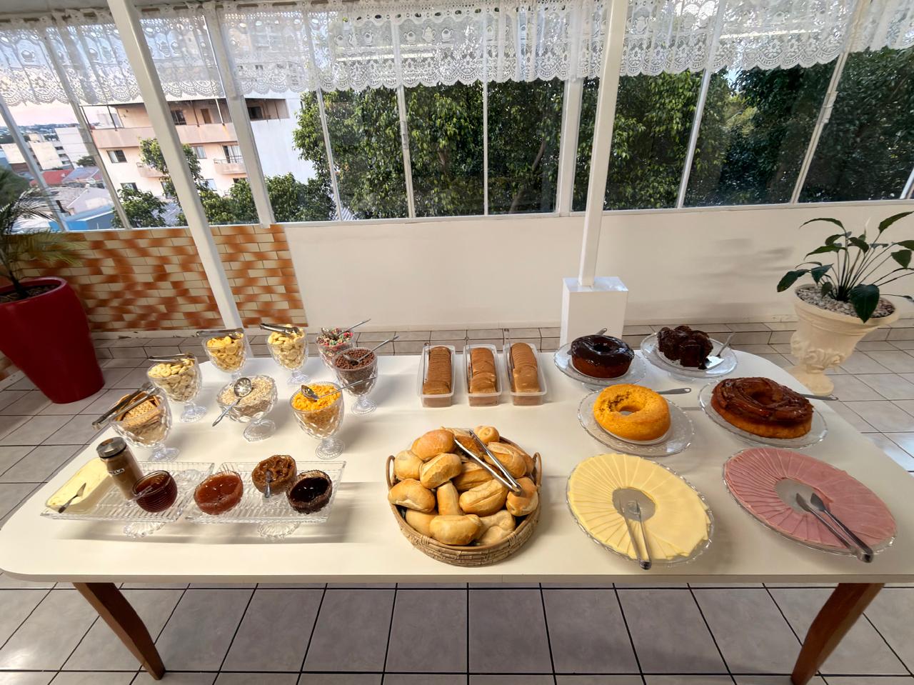 Mesa do café da manhã do Hotel Mello com pães, bolos, frios e cereais